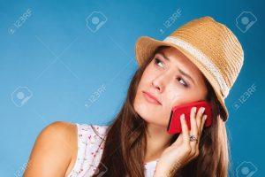Technology and communication - confused teen girl talking on mobile phone smartphone, worried woman using cell phone on blue. Misunderstanding.